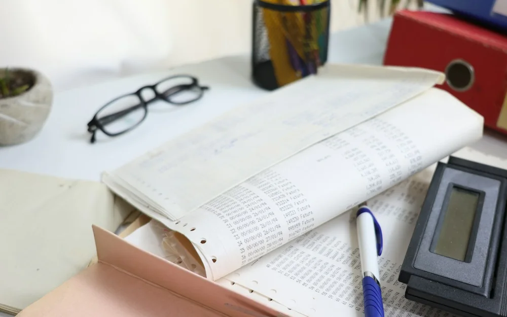 Printed accounting records beside a calculator, glasses and a pen.