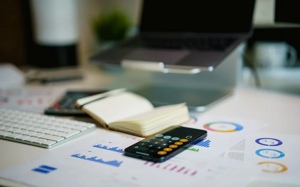 A phone calculator on printed charts beside a notebook and laptop.