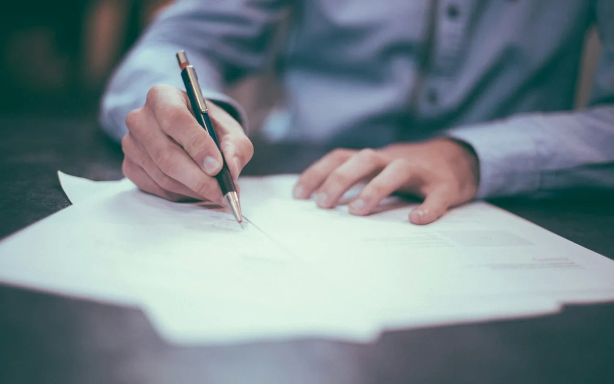 A hand completing a paper document with a pen.