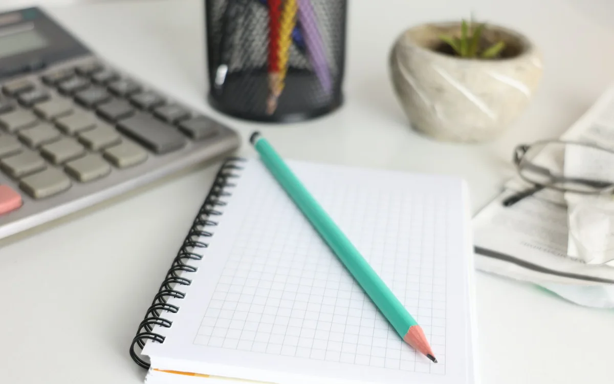 A calculator, notebook and pencil arranged on a desk.